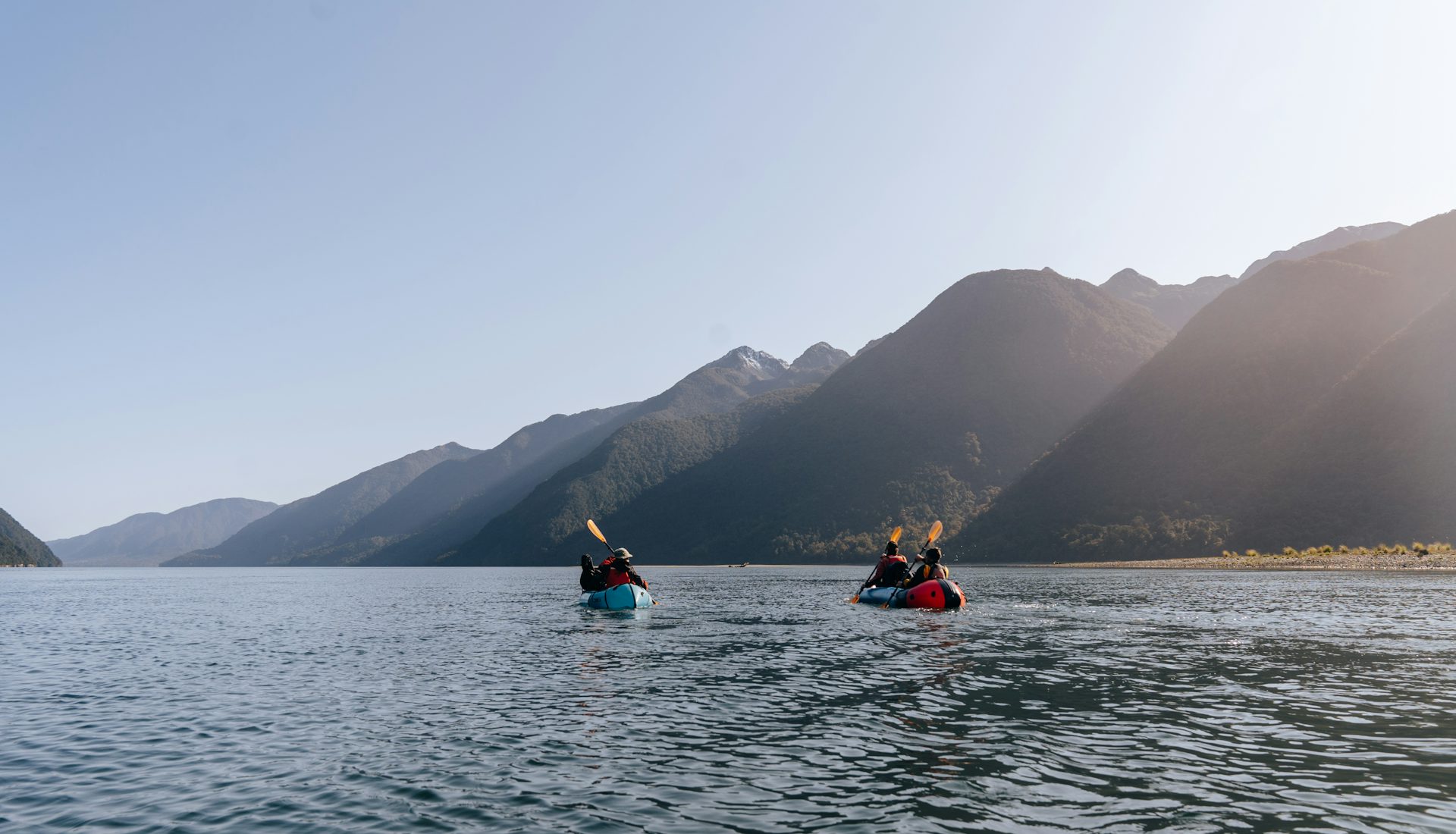 Two kayakers on a calm lake below the mountains